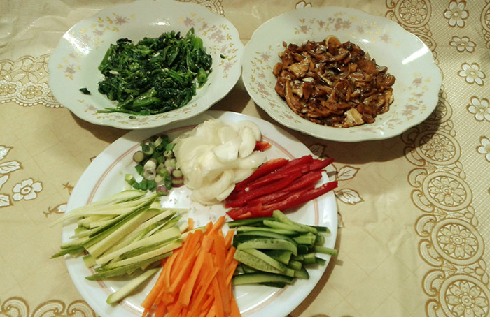  
Clockwise from left is blanched spinach with garlic, sesame oil and sesame seeds in the top-left plate; cooked mushrooms in the top-right plate, and carrots, zucchini, cucumber, bell pepper, and white and green onions in the bottom plate. 
